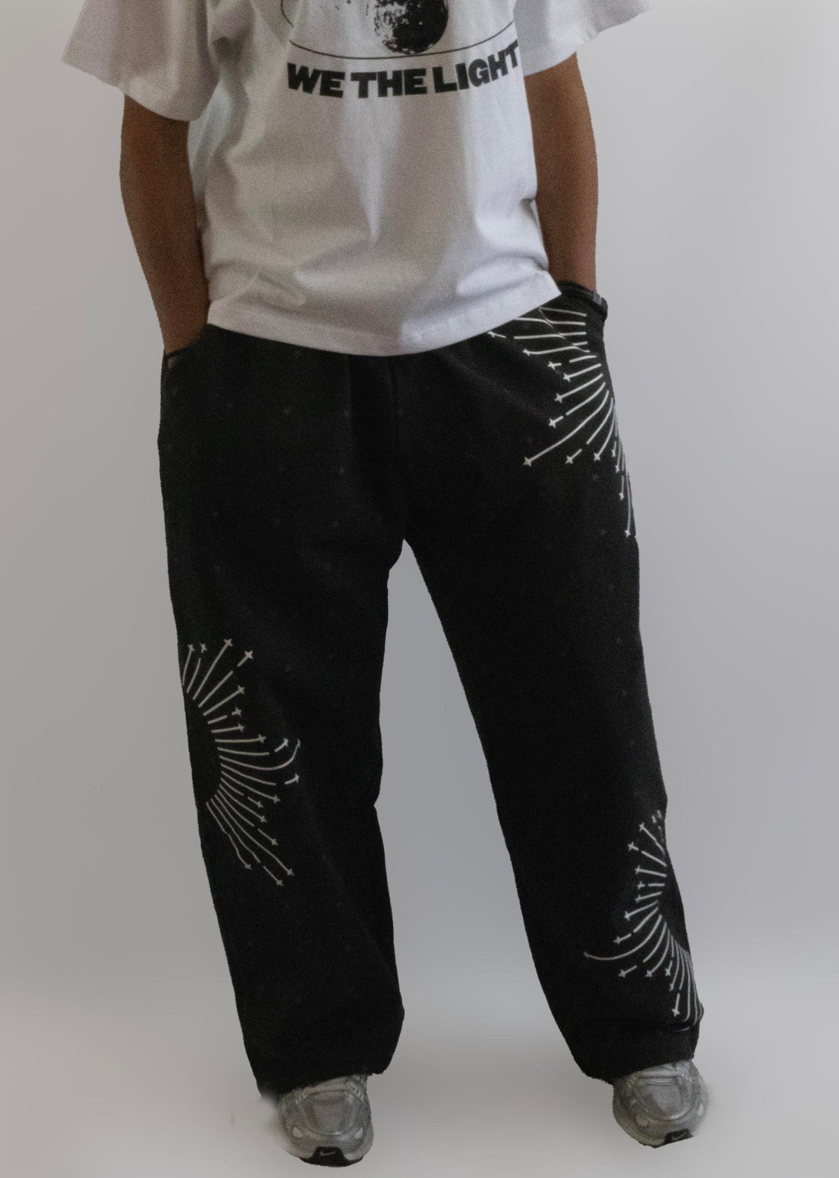 Person wearing a white t-shirt with text and black pants with white patterns on a plain background