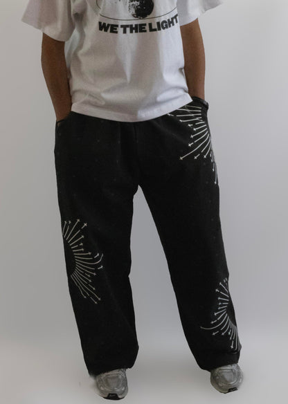 Person wearing a white t-shirt with text and black pants with white patterns on a plain background